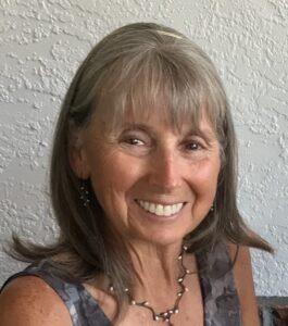 Smiling woman with gray hair against a textured wall.