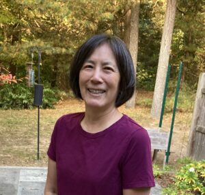 Smiling woman standing outdoors in a maroon shirt.