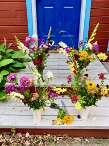 Two vibrant floral bouquets in white vases on a wooden porch.