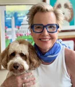 Smiling woman wearing blue glasses holding a fluffy dog.