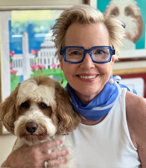 Smiling woman wearing blue glasses holding a fluffy dog.