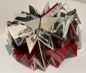 An intricate paper sculpture with folded pages and red accents.