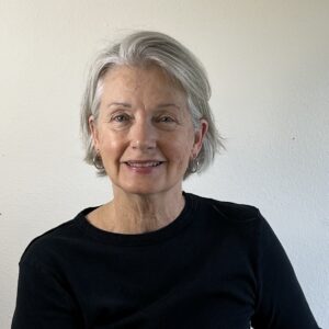 Smiling elderly woman with gray hair in a black top against a plain background.