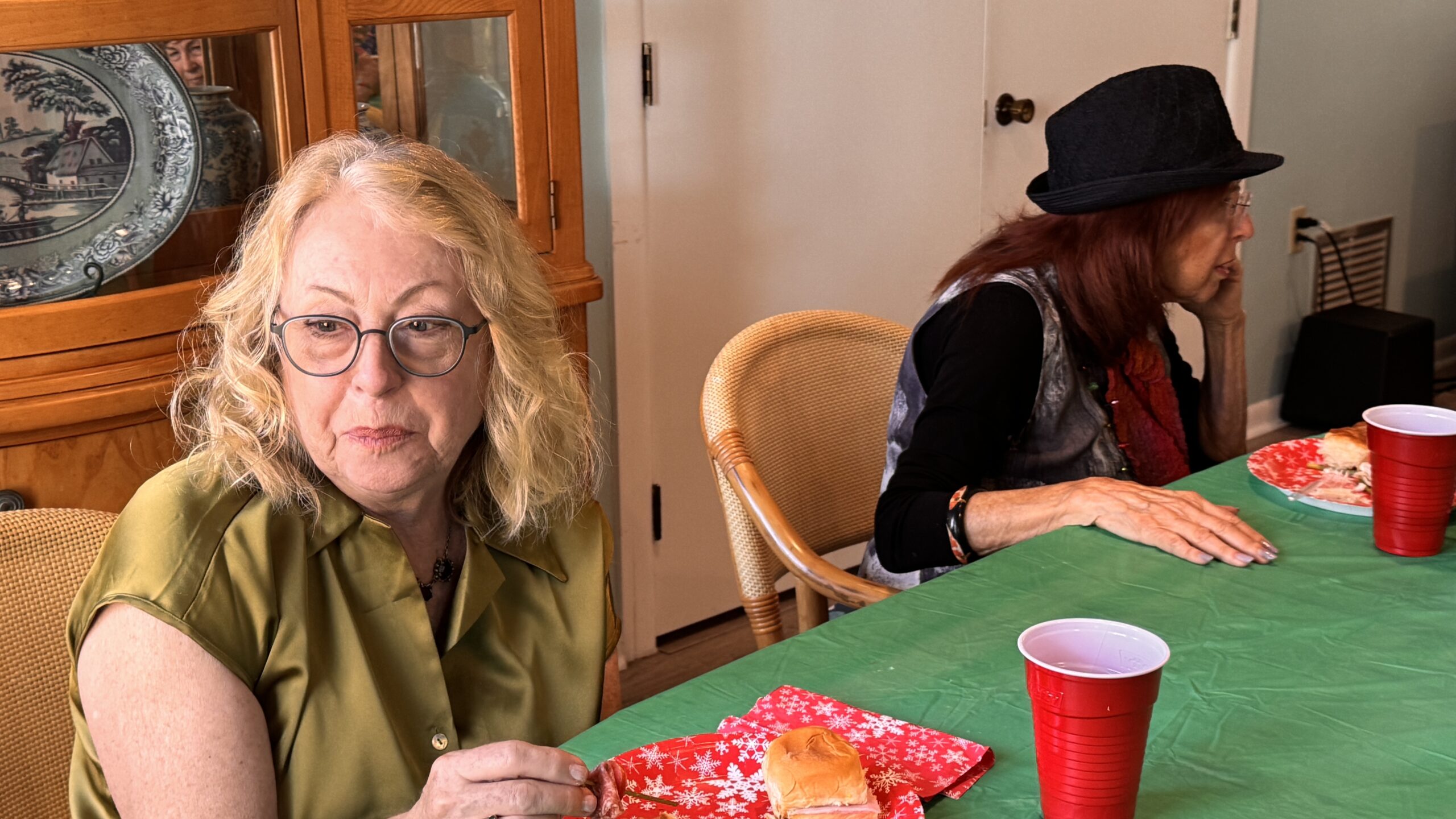 Two women sitting at a table with craft supplies and red cups.