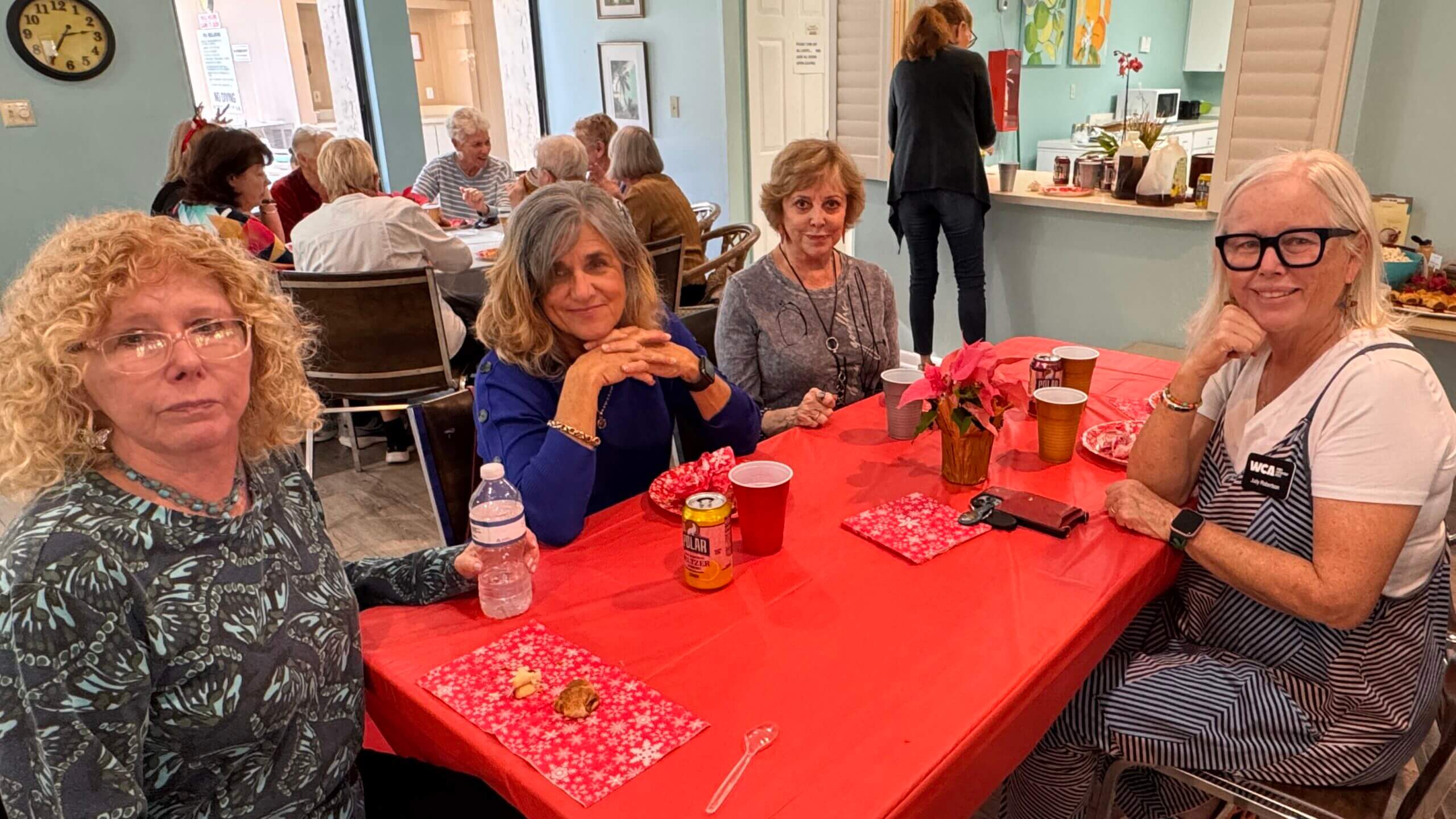 Two women sitting at a red-covered table with drinks and snacks in a cozy room.