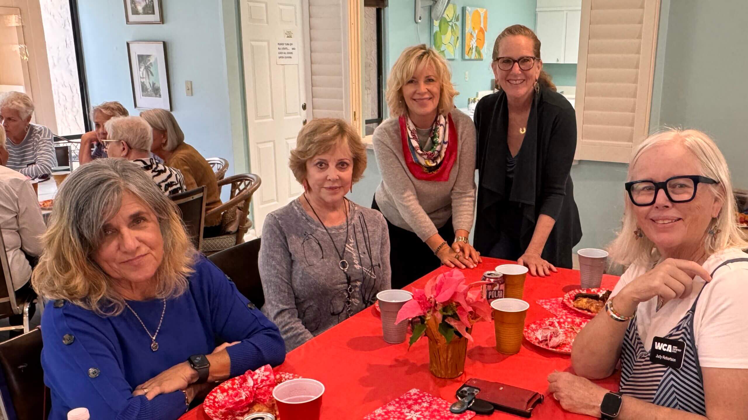 Four women gathered around a festive red table with poinsettia and coffee cups.