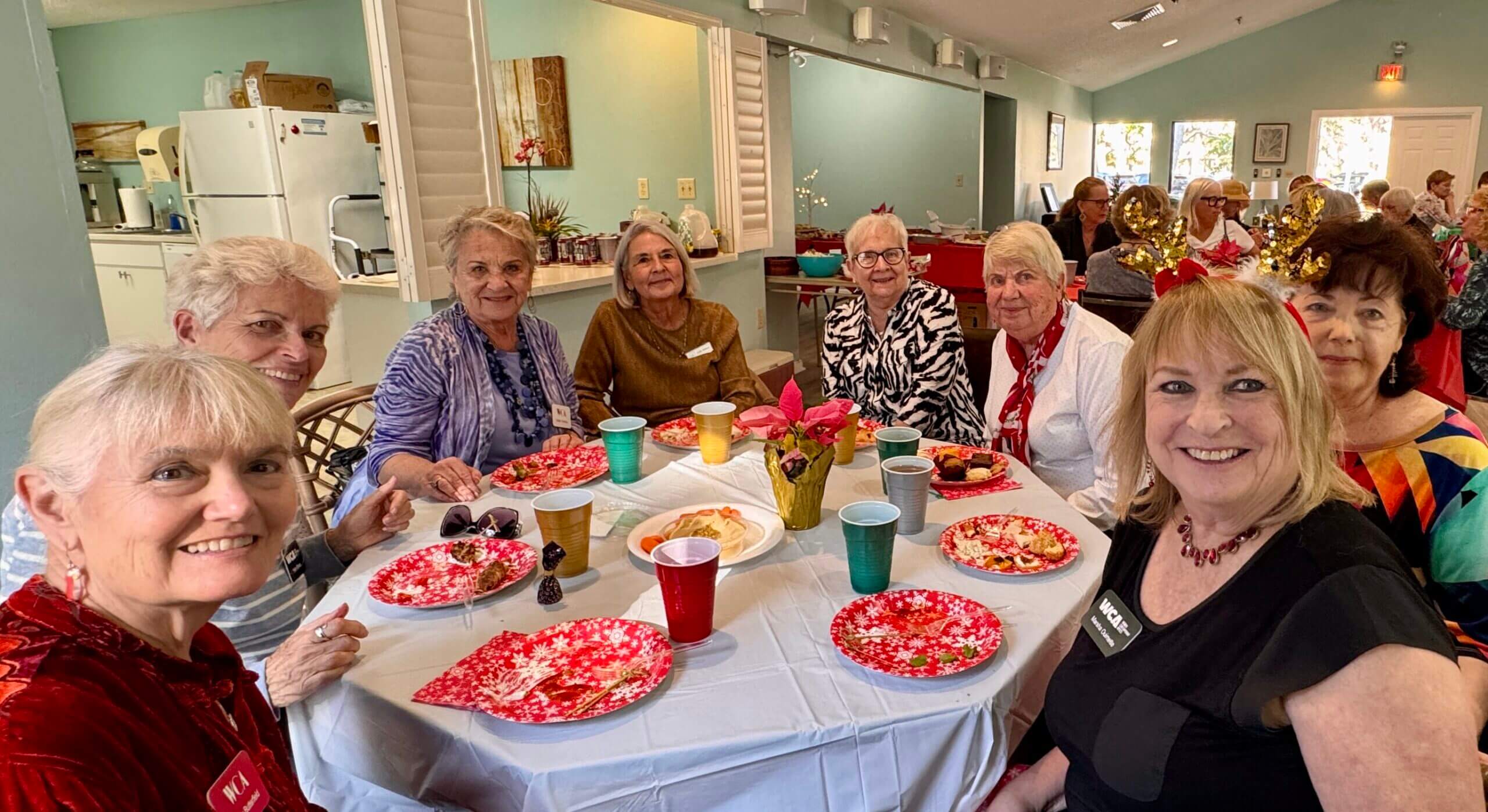 Four elderly women smiling around a table with food and drinks.