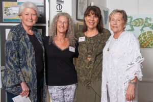 Four mature women standing together indoors, smiling.