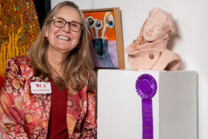 A smiling woman with an award-winning sculpture and purple ribbon.