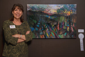 A woman stands confidently beside an abstract colorful painting in a gallery.