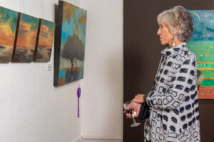 A woman observes paintings in an art gallery, holding a wine glass.