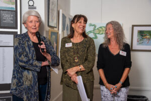 Three women engaged in conversation at an art gallery event.