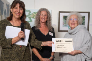 Three women smiling, one holding a certificate of appreciation.