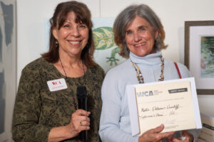 Two smiling women holding a microphone and a certificate.