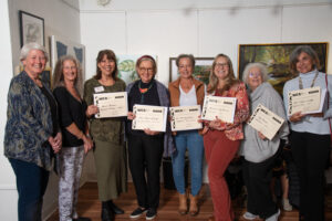 Group of six women holding certificates and smiling indoors.