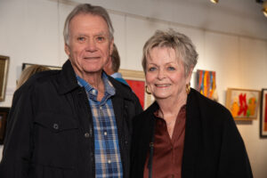 An elderly couple smiling indoors at an art exhibit.