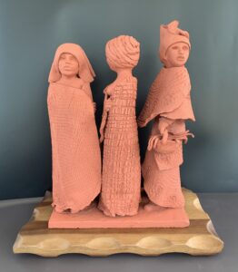 Three handmade clay figurines standing on a wooden base.