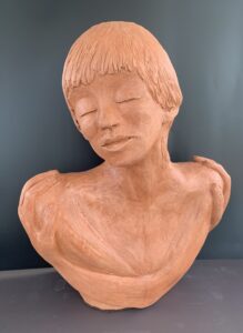 Terracotta bust of a serene young person with closed eyes and gentle features.