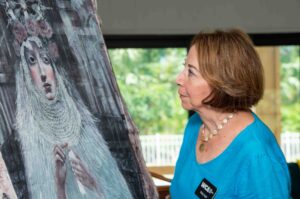 A woman attentively observes an artwork in a gallery setting.