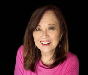 Smiling woman with shoulder-length brown hair wearing a bright pink top.